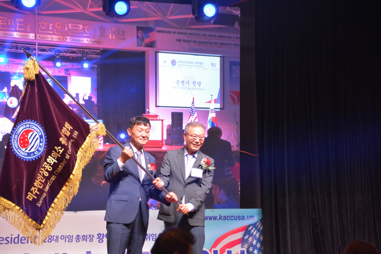 황병구 회장이 이경철 신임 회장(왼쪽)에게 미주한인상공회의소총연합회 깃발을 넘겨주고 있다.